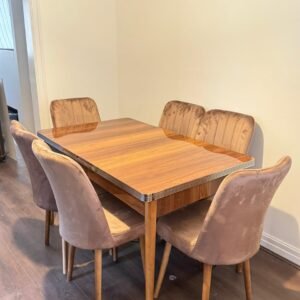 Dining table with six beige upholstered chairs in a room with light-colored walls and a wooden floor.