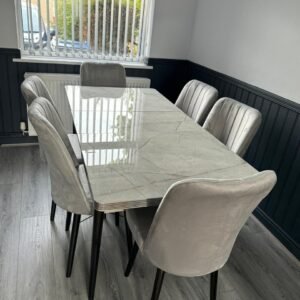Dining room with a glass-top table and six gray upholstered chairs near a window with white blinds.