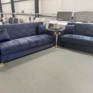 Two dark blue Alora Sofa Beds in a furniture showroom with gold accents and diamond quilted patterns.