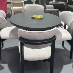 Aria Round Table Set with a dark tabletop and four light gray cushioned chairs in a showroom.