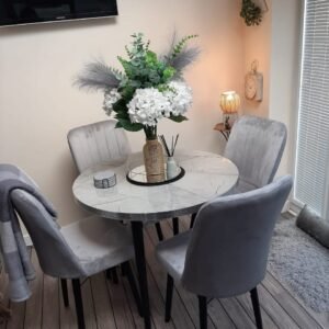 Dining area with round marble table, gray chairs, and flower vase.