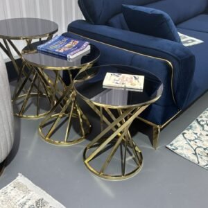 A pair of Canyon Coffee Tables with gold crisscross bases and dark glass tops beside a blue sofa and beige armchair.