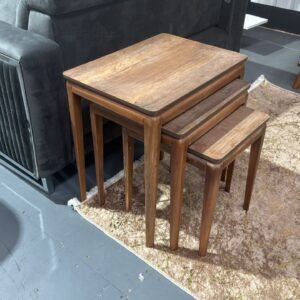 Set of three wooden nesting Edgewood Coffee Tables on a patterned rug beside a dark gray sofa.