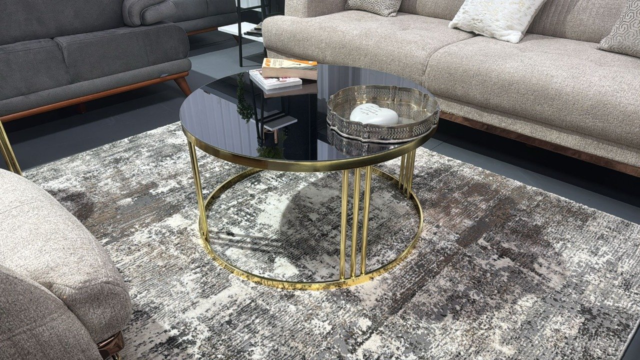 Elara Round Coffee Table with black glass and gold metal base in a living room.