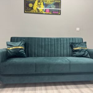 Emerald Luxe Sofa Bed in emerald green velvet with gold accents and decorative pillows, set against a grey wall.
