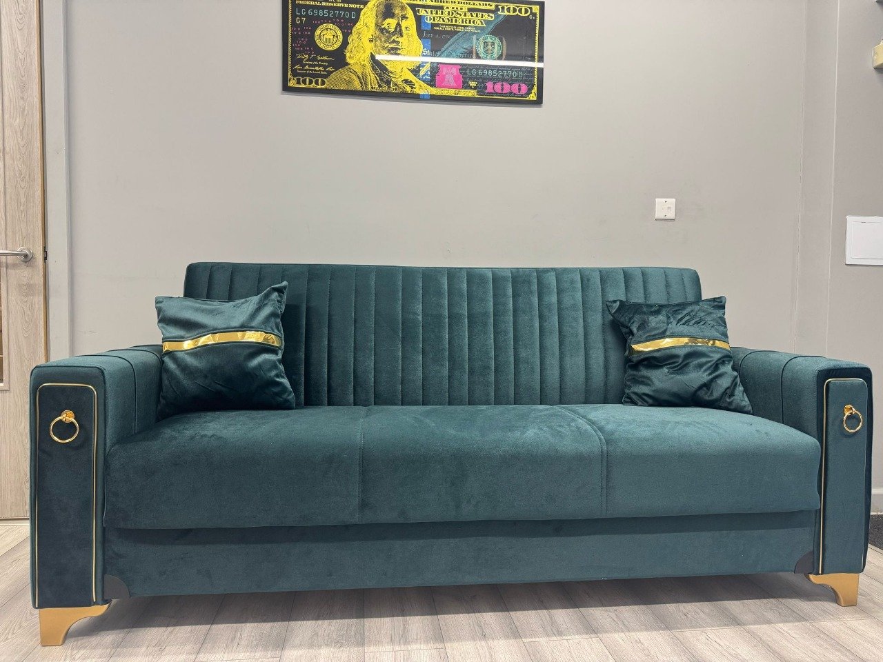 Emerald Luxe Sofa Bed in emerald green velvet with gold accents and decorative pillows, set against a grey wall.