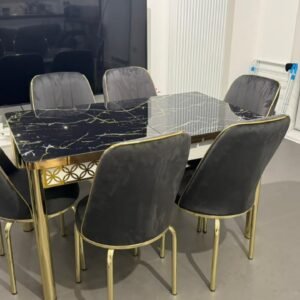 A dining area with a black marble table and six gray velvet chairs with gold accents.