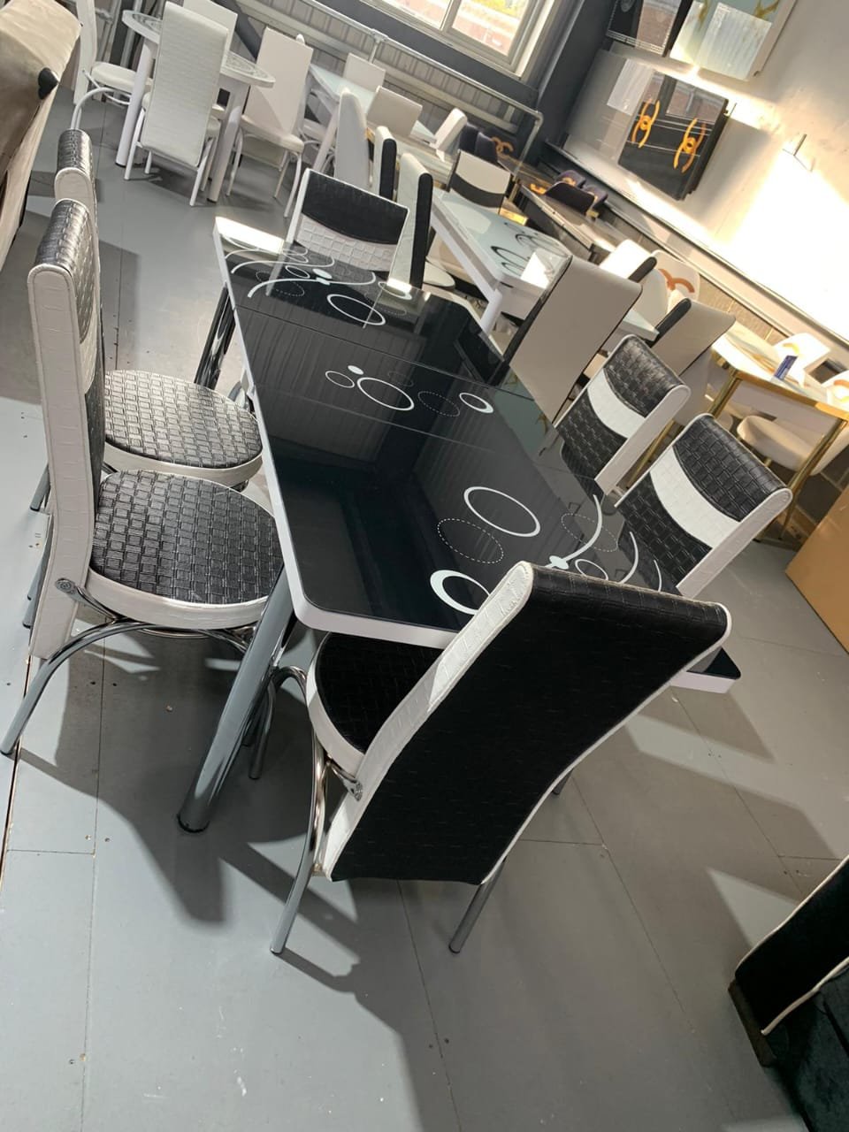 HaloStretch Dining Table with a black glass top and six matching chairs in a showroom.