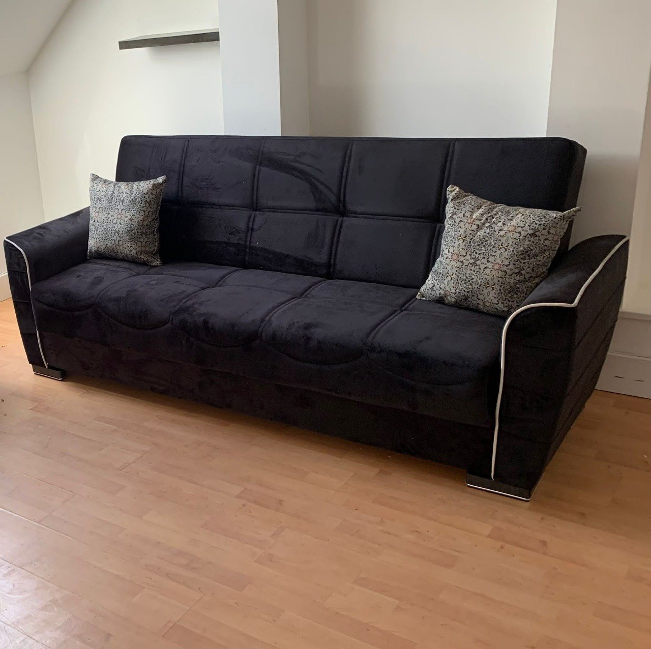 Jetform Sofa Bed with dark upholstery and two patterned cushions in a room with wooden flooring.