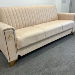 A beige Lucca Sofa Bed with vertical stitching and gold accents against a light-colored wall.