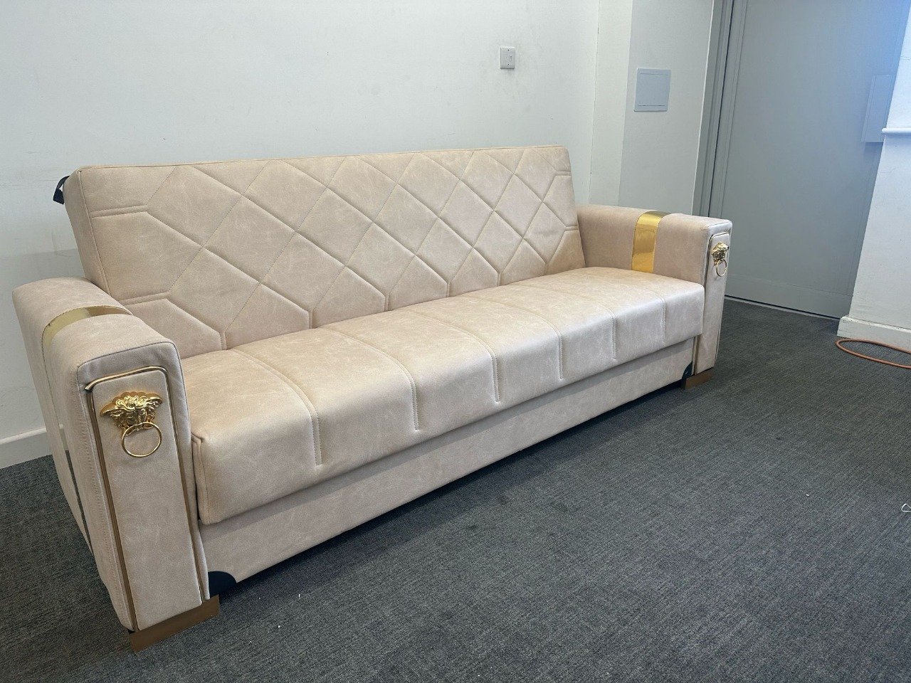 Lucca Sofa Bed in a minimalist room with light beige fabric and gold accents.