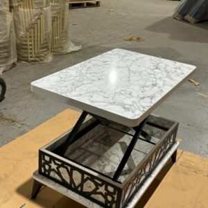A coffee table with a marble-like top and intricate black metal sides in a warehouse.