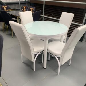 A round glass-top table with four white upholstered chairs, and dark chairs with gold accents in the background.
