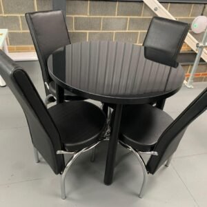 Round black table with four black chairs on a gray floor in an indoor setting.