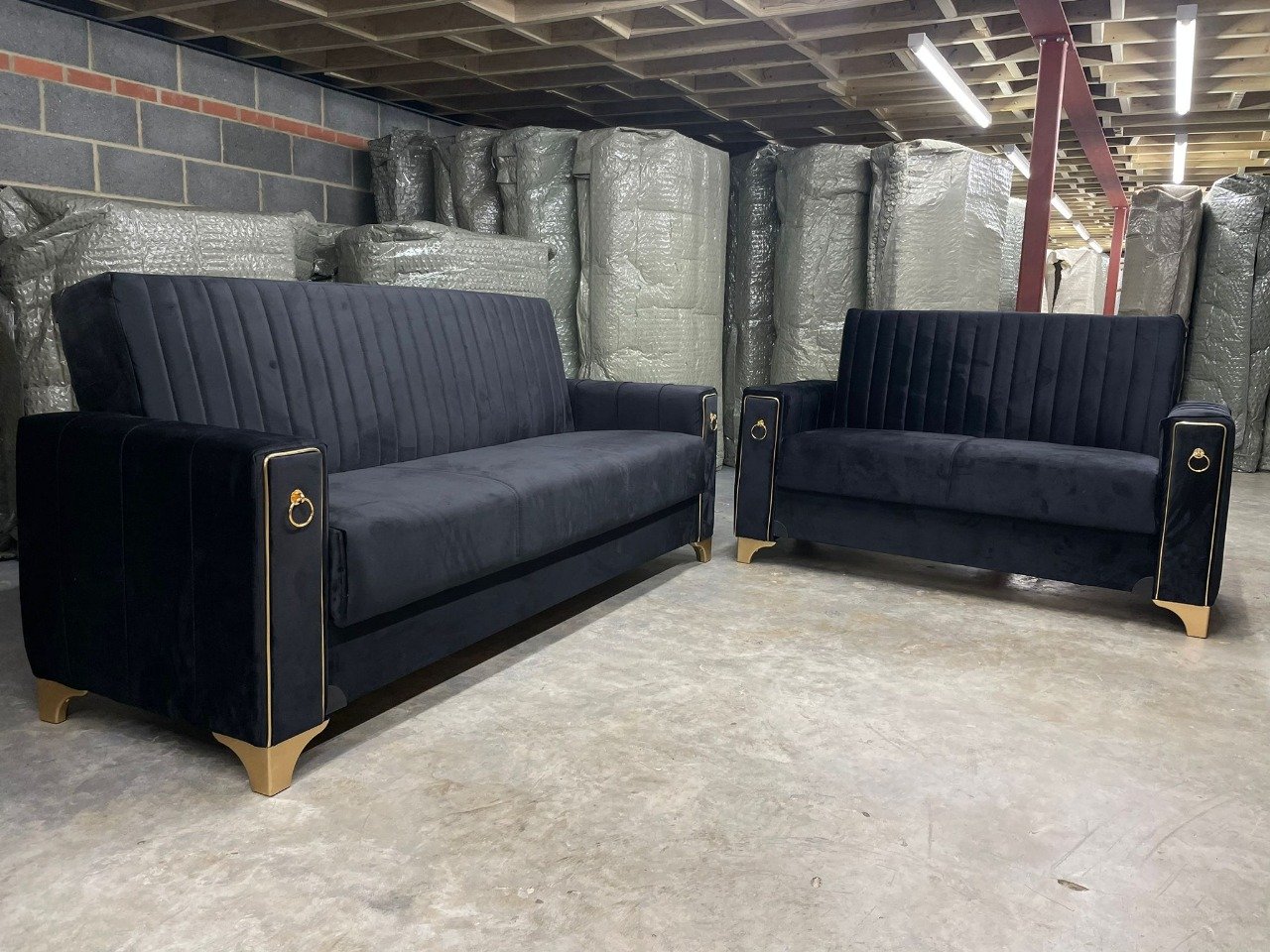 Two Midnight Velvet Sofa Beds with gold accents in an indoor storage space.