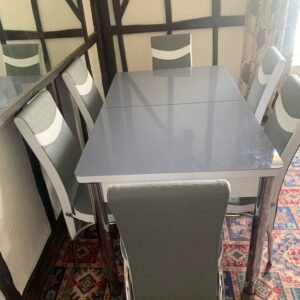 ModernVista Dining Set with gray table and four matching chairs in a room with black beams and colorful carpet.
