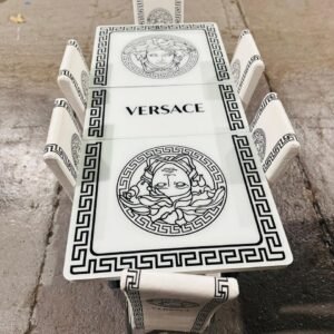 A rectangular dining table set with Greek key designs and Medusa motifs, labeled "VERSACE," on a concrete floor.