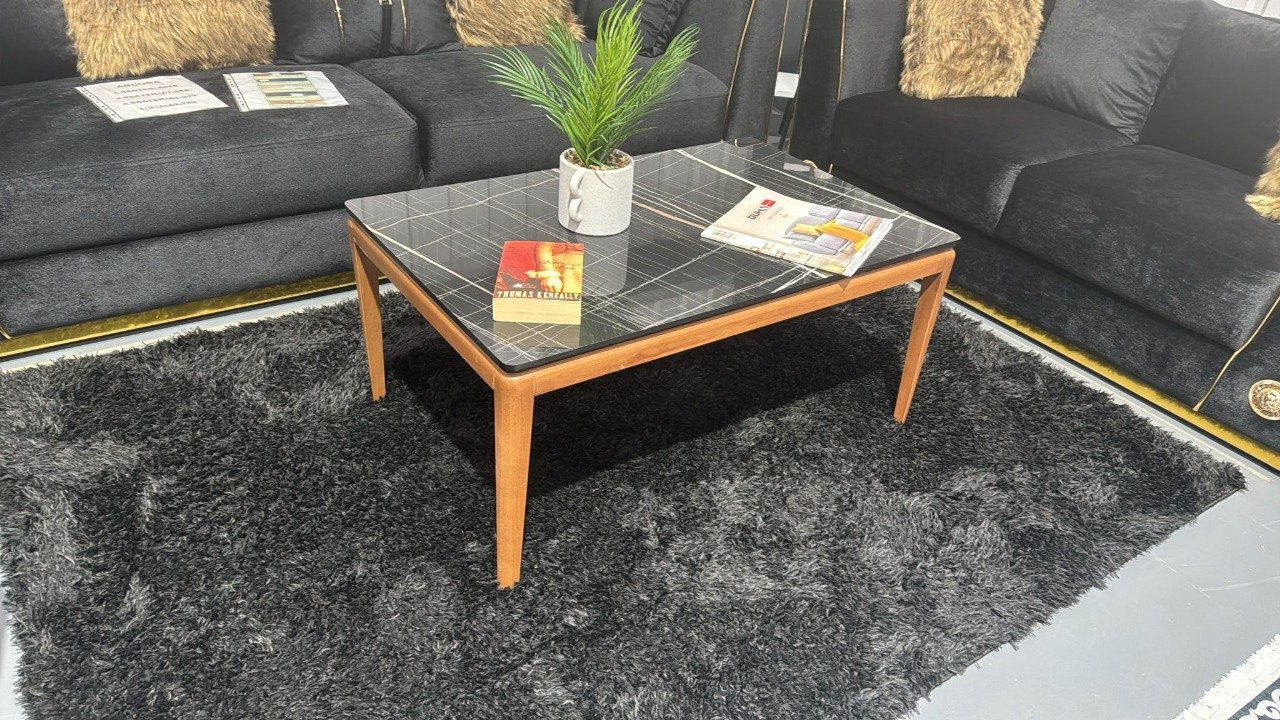 A Nora Coffee Table with a black checkered top and wooden legs, adorned with a plant and books, in a modern living room.