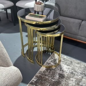 Nesting Quinn Coffee Tables with black glass tops and gold legs next to a grey sofa.