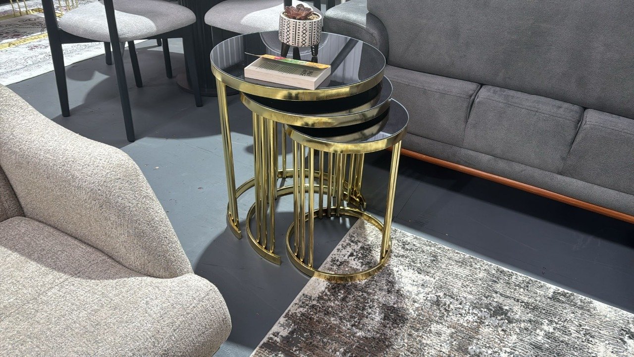 Nesting Quinn Coffee Tables with black glass tops and gold legs next to a grey sofa.