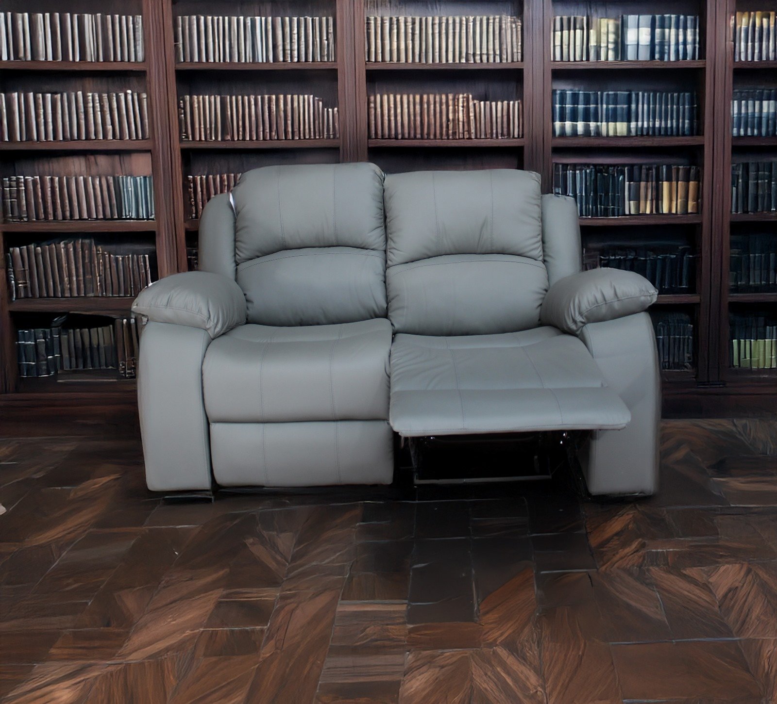 Gray leather sofa with a reclined footrest in front of a wooden bookshelf filled with books.