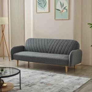 A modern living room with a gray sofa, tripod lamp, botanical artwork, round glass coffee table, and a large green plant.