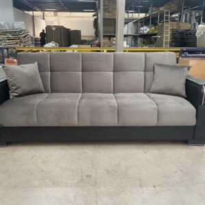 A three-seater gray sofa with black leather armrests in a warehouse.