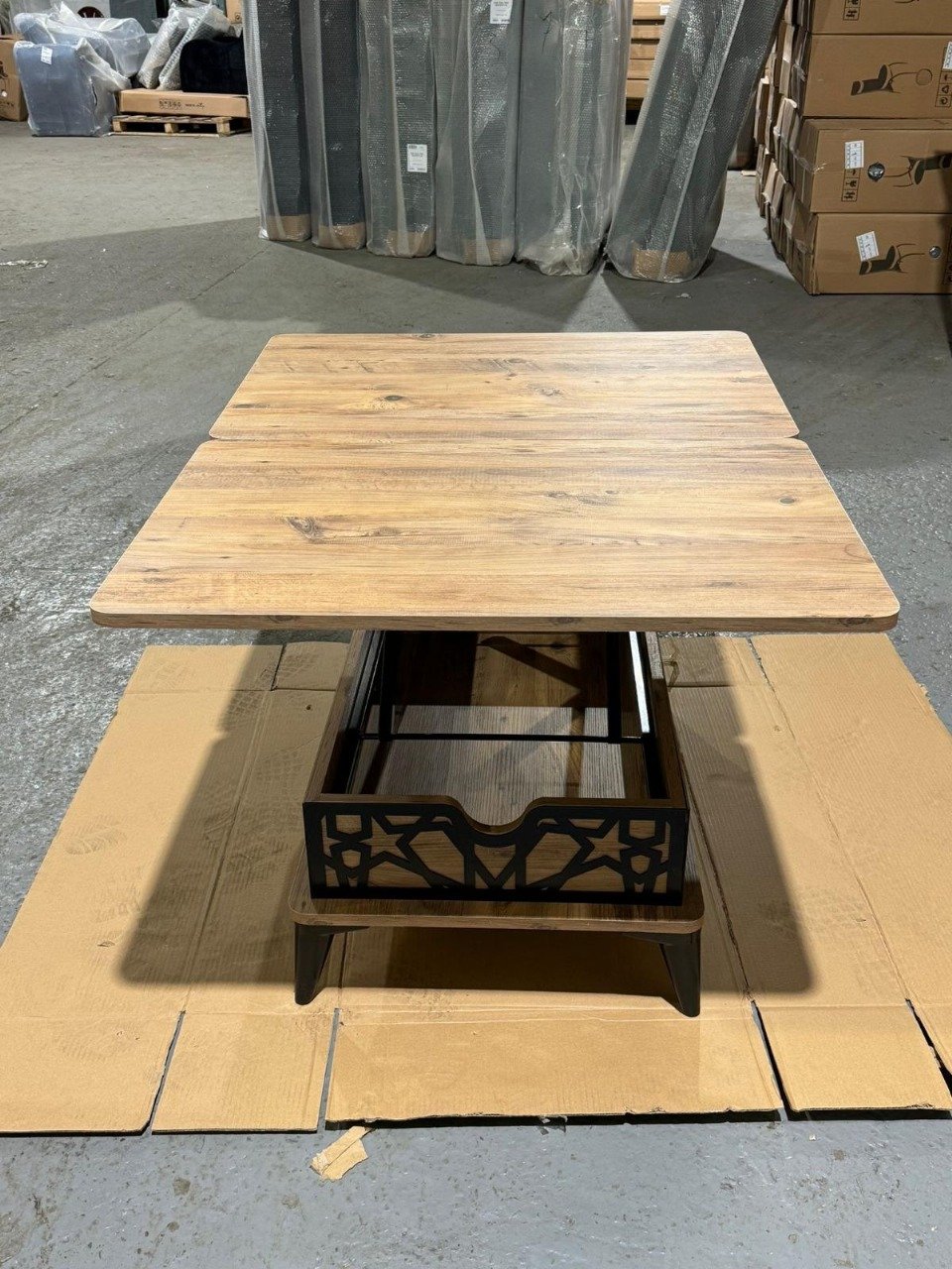 Wooden table with black metal accents on a cardboard base in a warehouse.