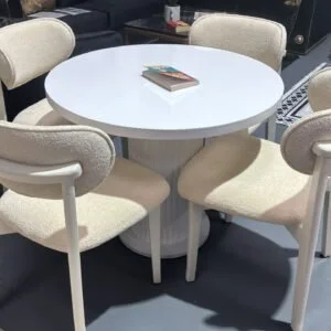 Aria Round Table Set with a white round table and four ivory upholstered chairs in a showroom.