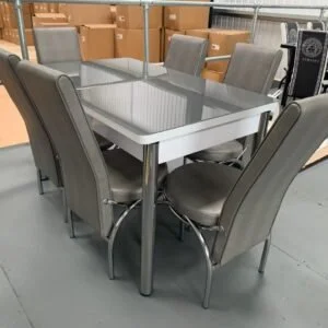 CrystalArc Extendable Dining Table with six gray upholstered chairs in a warehouse setting.